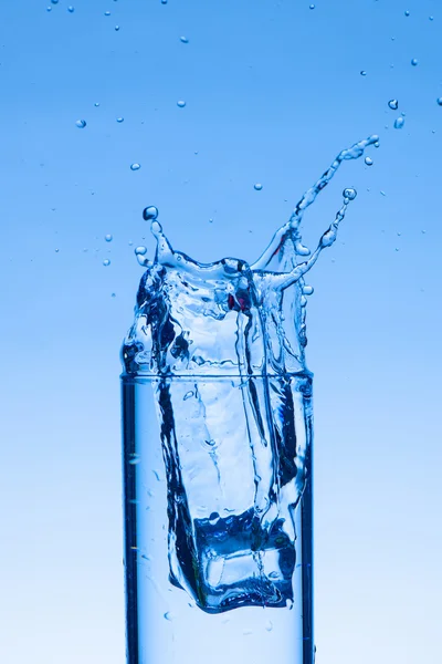 Ijsblokje valt in een glas water maken van een plons — Stockfoto