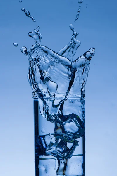 Ice cube tombe dans un verre d'eau créant un éclaboussure — Photo