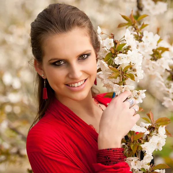 Mooie jonge vrouw met rode sjaal in park met kersenbloesem in het vroege voorjaar — Stockfoto