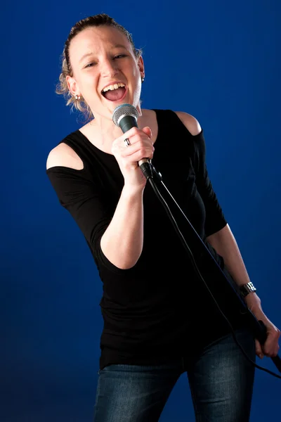 Mujer cantante sobre fondo azul con micrófono — Foto de Stock
