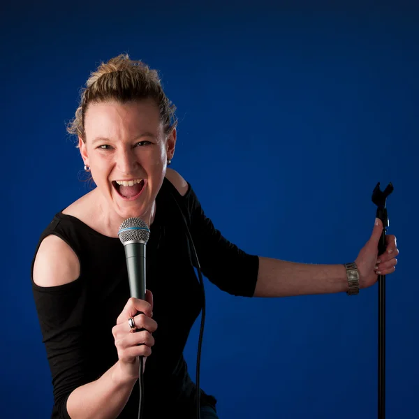 Γυναίκα τραγουδίστρια σε φόντο bluue με μικρόφωνο — Φωτογραφία Αρχείου