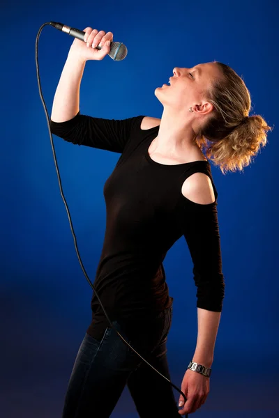Mujer cantante sobre fondo azul con micrófono — Foto de Stock