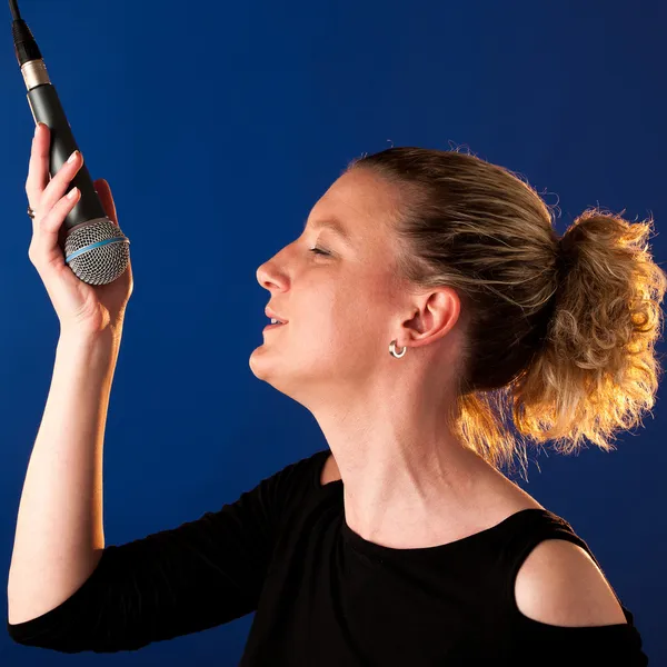 Piosenkarka kobieta na tle bluue z mikrofonem — Zdjęcie stockowe