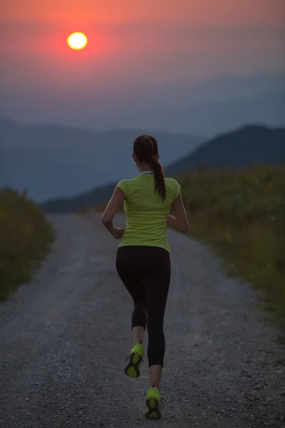 Mujer corriendo en un camino de montaña al atardecer de verano —  Fotos de Stock