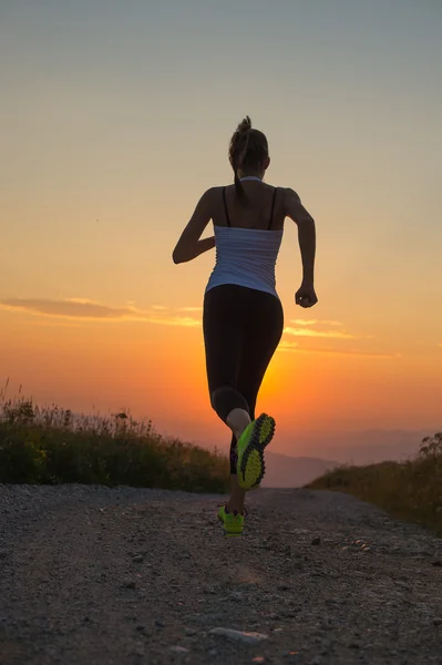 Frau läuft bei Sonnenuntergang auf einer Bergstraße — Stockfoto