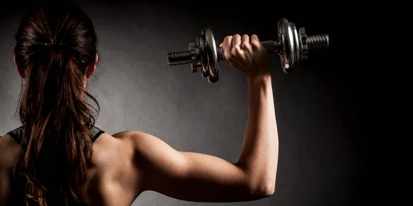 Atractive fit woman works out with dumbbells as a fitness conceptual over dark background.