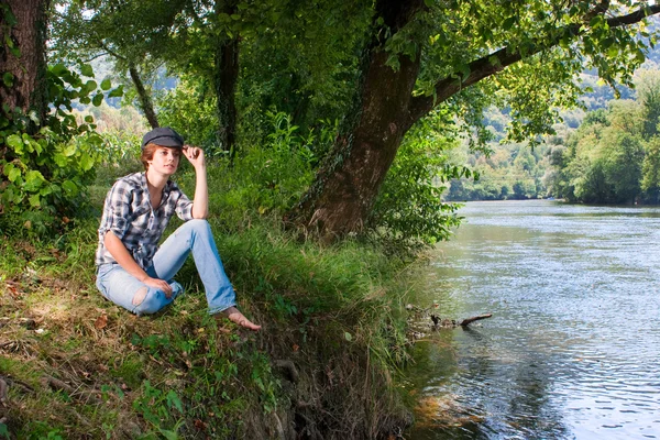 Krásná mladá žena sedí u řeky — Stock fotografie