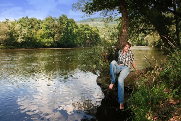 Krásná mladá žena sedí u řeky — Stock fotografie
