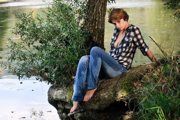 Schöne junge Frau sitzt am Fluss — Stockfoto