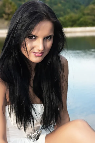 Krásná mladá žena sedí u jezera — Stock fotografie