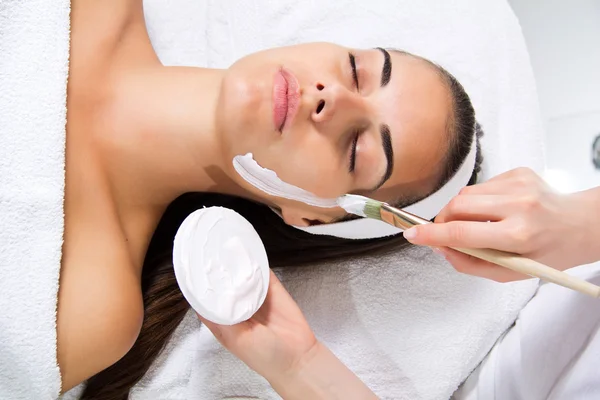 Beautiful young woman getting facial mask — Stock Photo, Image