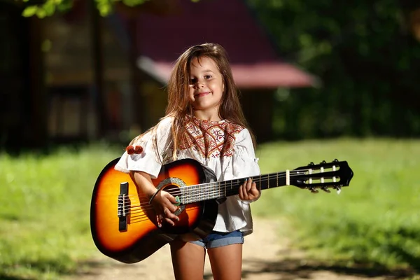 一个手里拿着吉他的漂亮小女孩在大自然中装腔作势 享受夏天的一天 — 图库照片