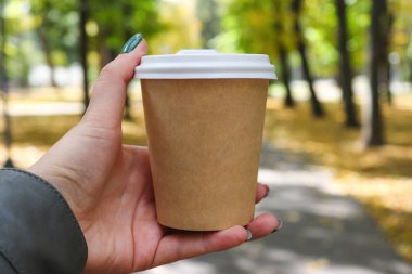 Arka planda bulanık sonbahar yeşilliği ve metin için fotokopi alanı olan bir fincan kahve tutan kadın..