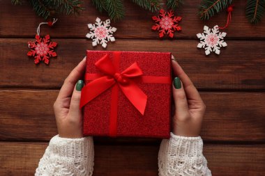 Dişi eller, Noel ağacı dalları ve süslemeleri olan bir hediye kutusunu ahşap masada tutuyorlar. Üst manzara, düz uzanma.