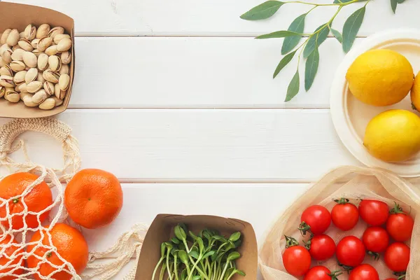 Mikroyeşil, kiraz domatesleri, mandalinalar, fıstıklar ve limonlar beyaz ahşap masa üzerinde fotokopi alanı ile. Taze sağlıklı organik gıdalar ve tek kullanımlık organik aletler. Vejetaryen yemeği. Sıfır atık