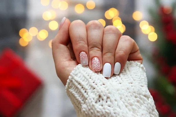 A téli manikűr ötlete. Nők kéz gél lengyel manikűr fehér színű és hópelyhek dísz ünnepi karácsonyi háttér ellen. Szelektív fókusz — Stock Fotó