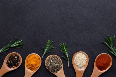 Ahşap kaşıklardaki çeşitli baharat ve otlar fotokopi alanı olan karanlık bir arka planda. Paprika, zerdeçal, kurutulmuş zencefil, kurutulmuş otlar ve biber karışımı. Üst görünüm.