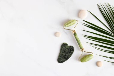 Yeşim yüz silindiri ve mermer masaya masaj için taş. Geleneksel Çin yüz masajı için özel cihazlar, Gua Sha. Üst manzara, düz uzanma.