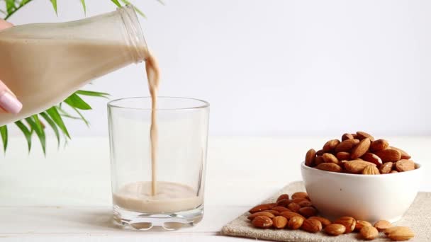 Badem sütü masanın üzerine bir içki bardağına dökülüyor. Vejetaryen bitkisel gıda. Sağlıklı gıda konsepti, laktozsuz yiyecek. — Stok video