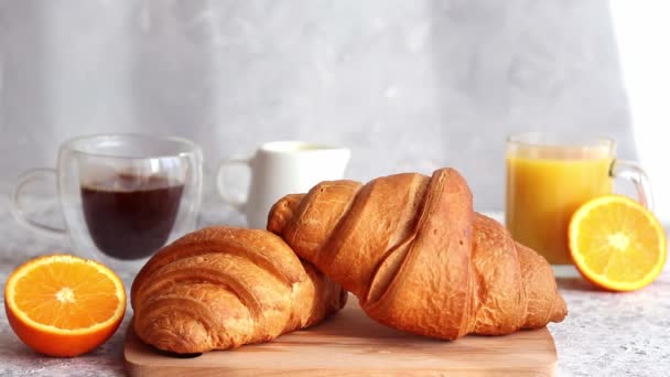 Výborná koncepce snídaně. Croissanty s pomerančovým džusem a kávou na stole. Ženská ruka nalévá mléko do sklenice kávy. Selektivní zaměření — Stock video