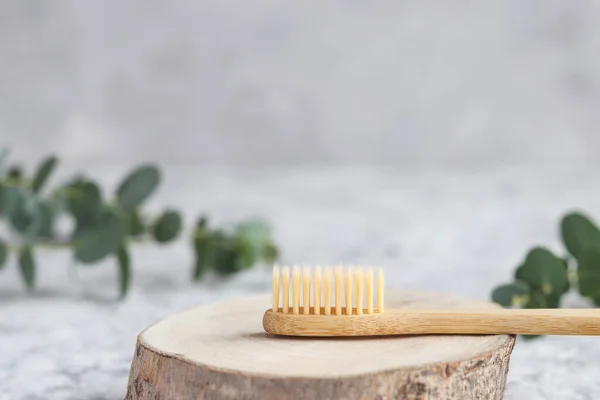 Eco-friendly bamboo toothbrush on a wood cut and eucalyptus leaf against grey wall with copy space. Oral hygiene and zero waste concept. Selective focus — Stock Photo, Image