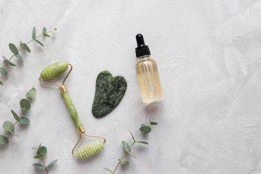 Yeşim yüz silindiri, masaj için taş ve gri desenli masada gerekli yağ. Gua Sha için özel cihazlar. Geleneksel Çin yüz masajı. Güzellik ve sağlık hizmeti konsepti. Üst görünüm, alanı kopyala