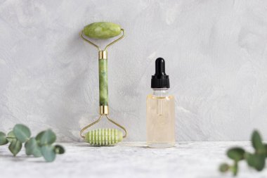 Gua Sha masajı için aletler. Yeşim yüzlü silindir ve gri desenli duvara karşı gerekli yağ. Geleneksel Çin yüz masajı. Güzellik ve sağlık hizmeti konsepti. Seçici odak