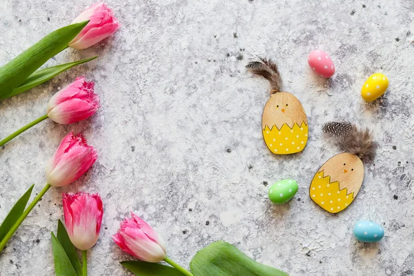 Easter composition with pink tulips, wooden chicken toys, colorful eggs and copy space against grey textured background. Top view, flat lay — Stock Photo, Image