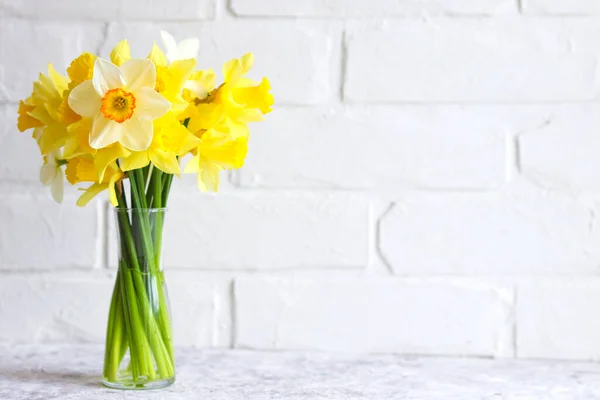 Bouquet of yellow daffodils in a vase against a brick wall. Flower arrangement. Greeting card for the holidays. Minimalism 스톡 사진
