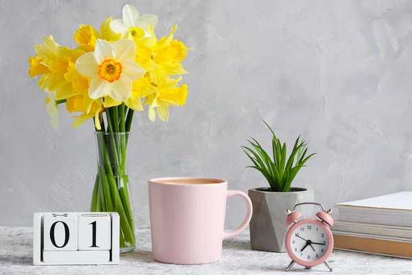 Table with succulent plant, bouquet of daffodils, alarm clock, cup of coffee, calendar with empty space for month and books. Morning concept. Home design — Stock Photo, Image