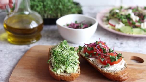 Womans hand pouring olive oil to fresh homemade toasts with microgreens, avocado, and tomatoes. Healthy food and dieting concept — Vídeos de Stock
