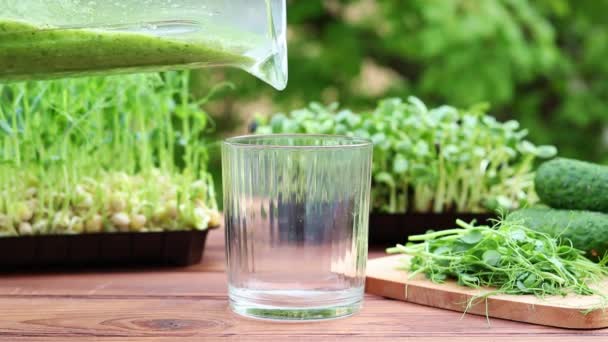 Zelený zeleninový koktejl se nalévá do sklenice na pozadí zeleně a mikrozeleně. Zdravé, veganské jídlo, dietní koncept. Selektivní zaměření — Stock video