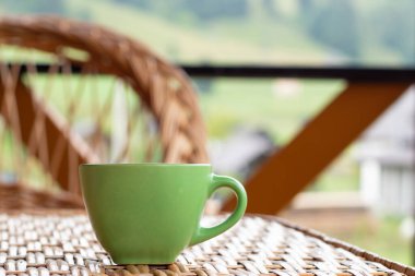 Green cup of coffee or tea on the terrace against nature background. Nature concept, relaxation.