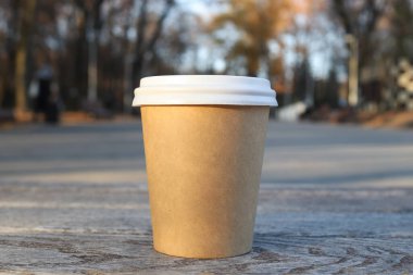 Mock up with empty cup of coffee on bench against background of blurred autumn park. Copy space, selective focus.