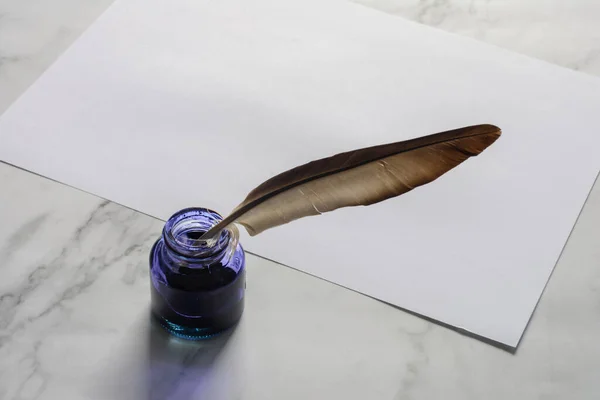Feather pen, Blue ink bottle  and plain white paper on marble table background.