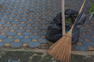 Coconut broom and black biodegradable trash bag on natural light background.