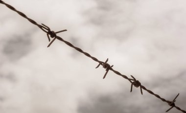 Old rusty barbed wire against blurred sky with clouds background.
