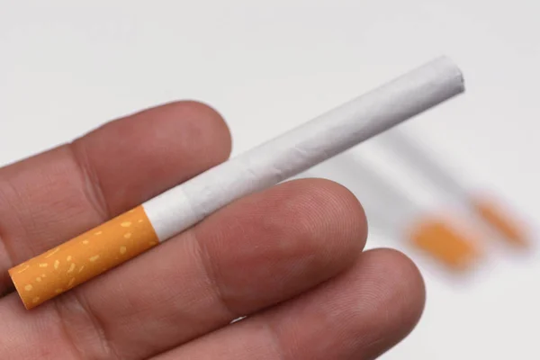 Human finger holding cigarette on natural white background.
