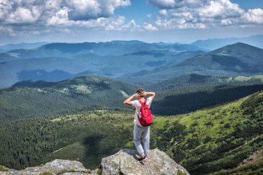tourist hiker with a backpack on top of a mountain in summer stands at a height and looks the green valley