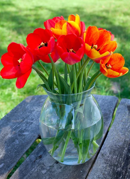 Tulipes dans un vase en verre sur table de jardin — Photo