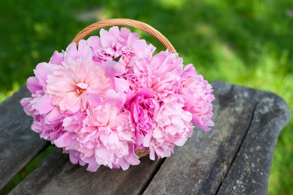 Bunch of peonies in a basket on wooden background — Stock Photo, Image