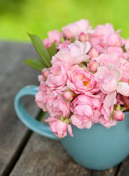 Taza azul llena de pequeñas rosas rosadas — Foto de Stock