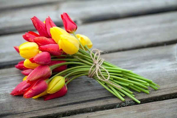 Прив'язані жовті і червоні тюльпани на дерев'яній поверхні — стокове фото