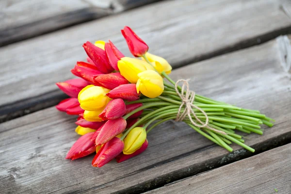 Tulipanes amarillos y rojos atados en superficie de madera — Foto de Stock