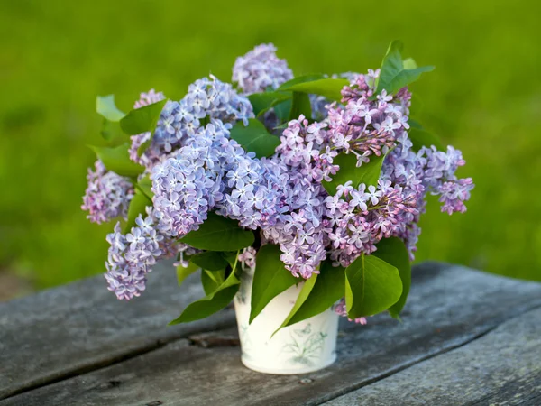Bucket with lilac flowers on wooden garden table — Stock Photo, Image