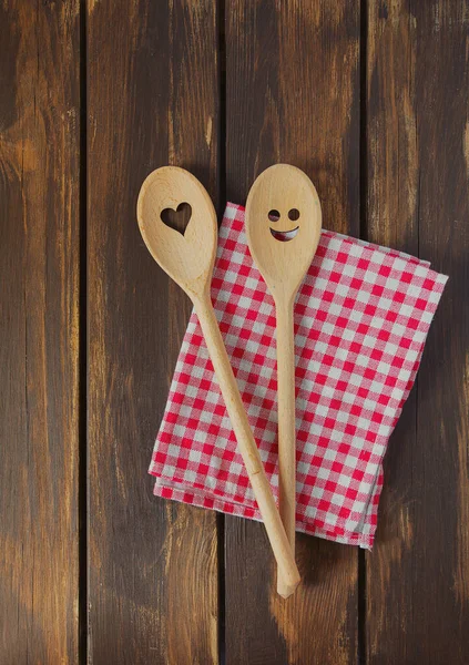 Two wooden spoons on brown wooden surface. Cooking concept. Spoons are with a smile and heart on it.