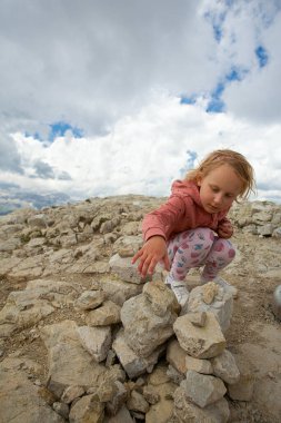 cute girl is building a stone pyramid in mountains
