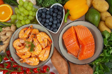 karides, somon filetosu ve taze sebze ve meyveler etrafına dizilmiş, üst manzara.