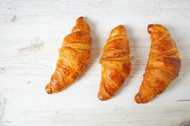 Beyaz ahşap yüzeyde yatan üç kruvasan.