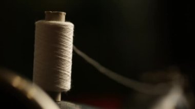 Eski bir dikiş makinesinin üzerinde koyu renklerde beyaz bir iplik topu.